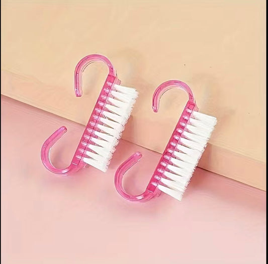 Dual pink nail cleaning brushes on a pastel pink background.